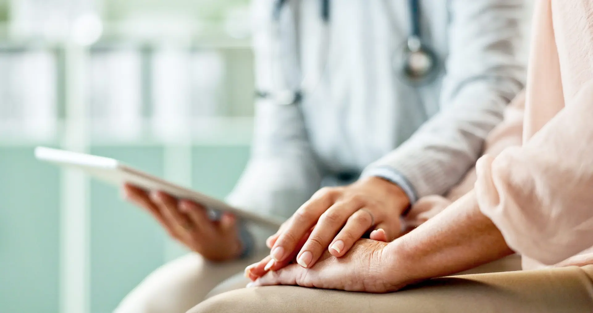 A doctor holds a patient's hands while reviewing a tablet
