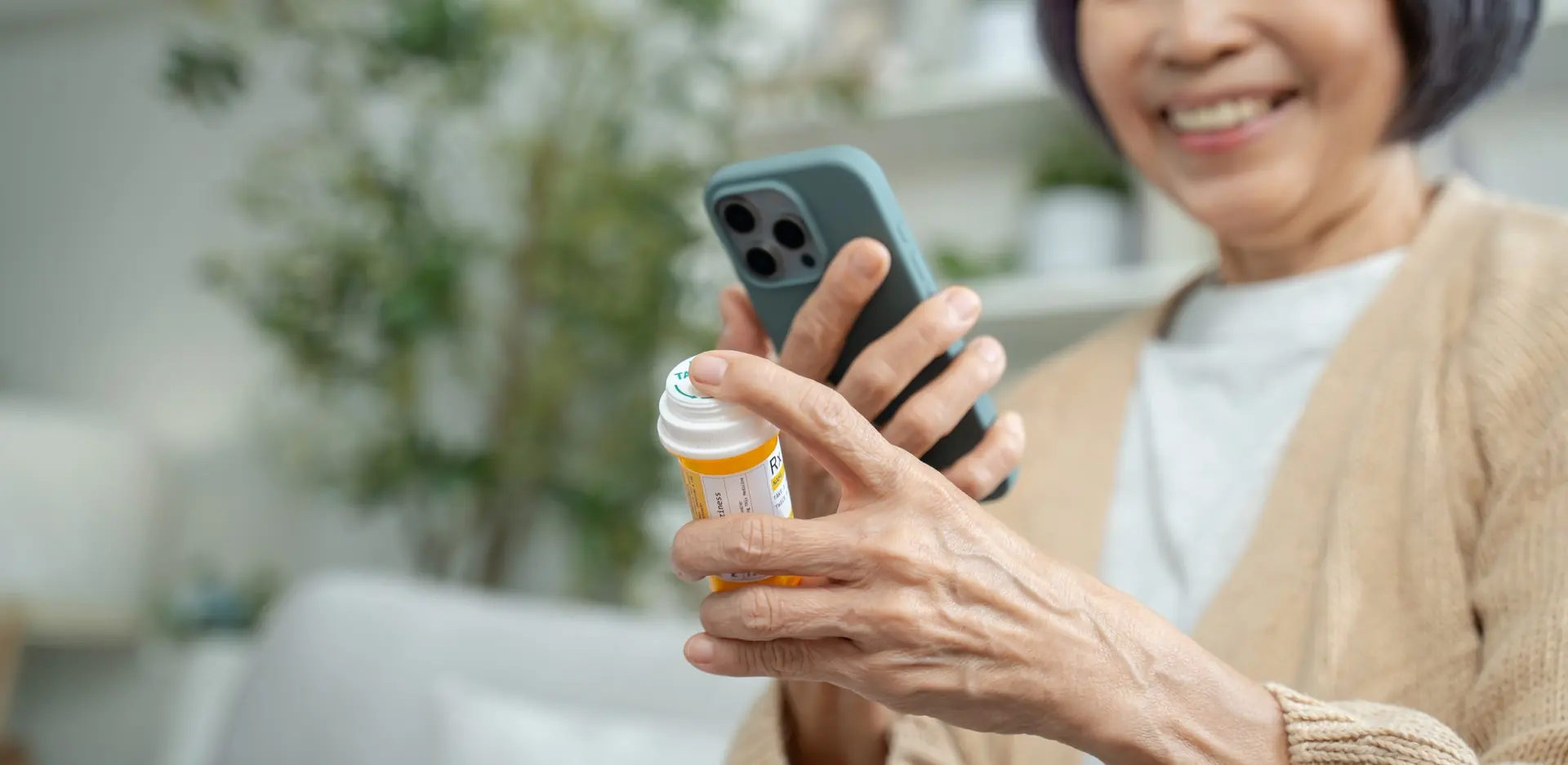 A smiling older woman at home checks her medication and her phone